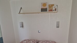 Une chambre à coucher avec un lit, deux oreillers, une table de chevet et une étagère murale décorée de tableaux.