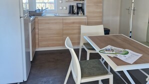 Une cuisine compacte avec un coin repas, comprenant une table avec des chaises, un réfrigérateur et une fenêtre laissant entrer la lumière naturelle.