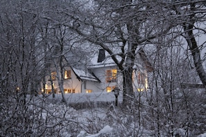 Paisagem coberta de neve com um edifício com várias janelas e uma varanda visível.