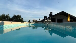 A clear swimming pool with a ladder, a building with a garage, and trees in the background. - Apartment 'Ferienwohnung Waldblick' with Private Pool, Private Terrace and Wi-Fi (Thurmansbang)