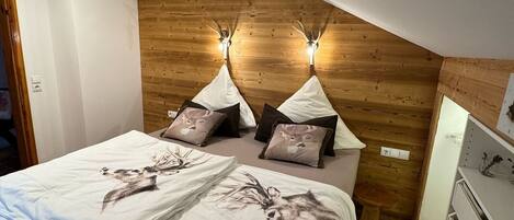 Un dormitorio con cama, almohadas, cabecera de madera, luces fijadas a la pared y cómoda.