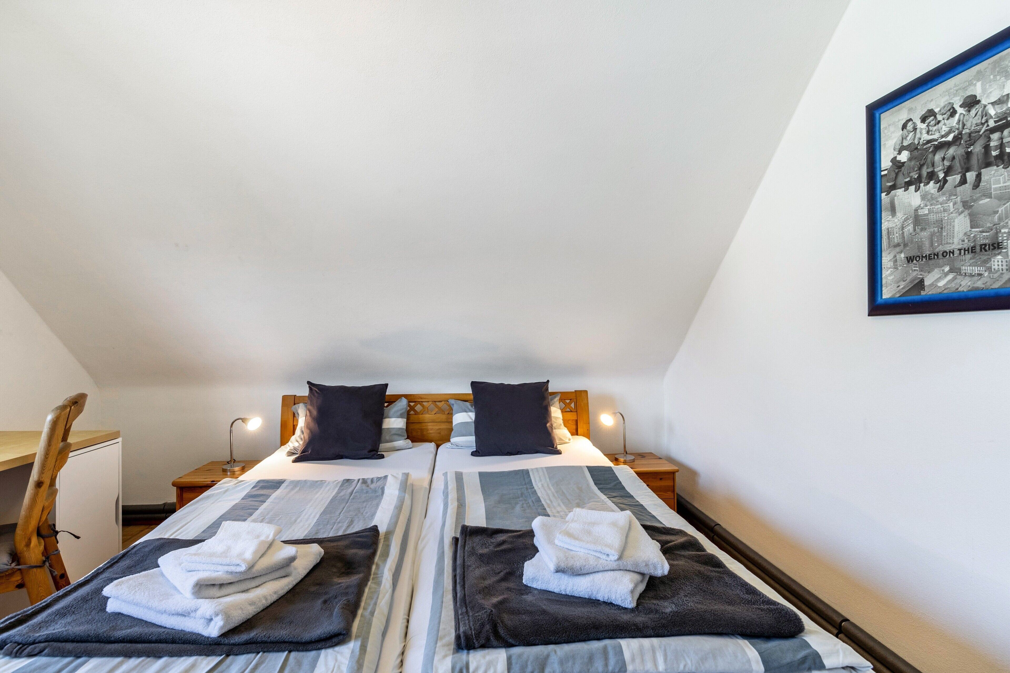 A twin room with two beds, a desk, and a framed picture on the wall.