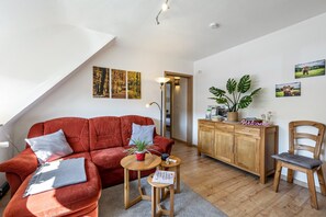 Ein Wohnzimmer mit einem roten Sofa, einem Holzschrank, einem Holzstuhl und einem kleinen Tisch mit einer Pflanze.