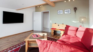 Un salon moderne avec un téléviseur à écran plat, un canapé rouge, une table basse en bois et un banc en bois.