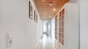 Un couloir aux murs blancs, au plafond en bois et au sol carrelé.