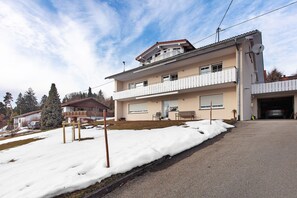 A two-story residential building with a balcony, a garage, and a snow-covered driveway. - Apartment 'Haus Eckert' with Balcony and Wi-Fi (Höchenschwand)