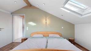 Une chambre avec un plafond en pente, un puits de lumière, un cadre de lit en bois et une table de chevet.