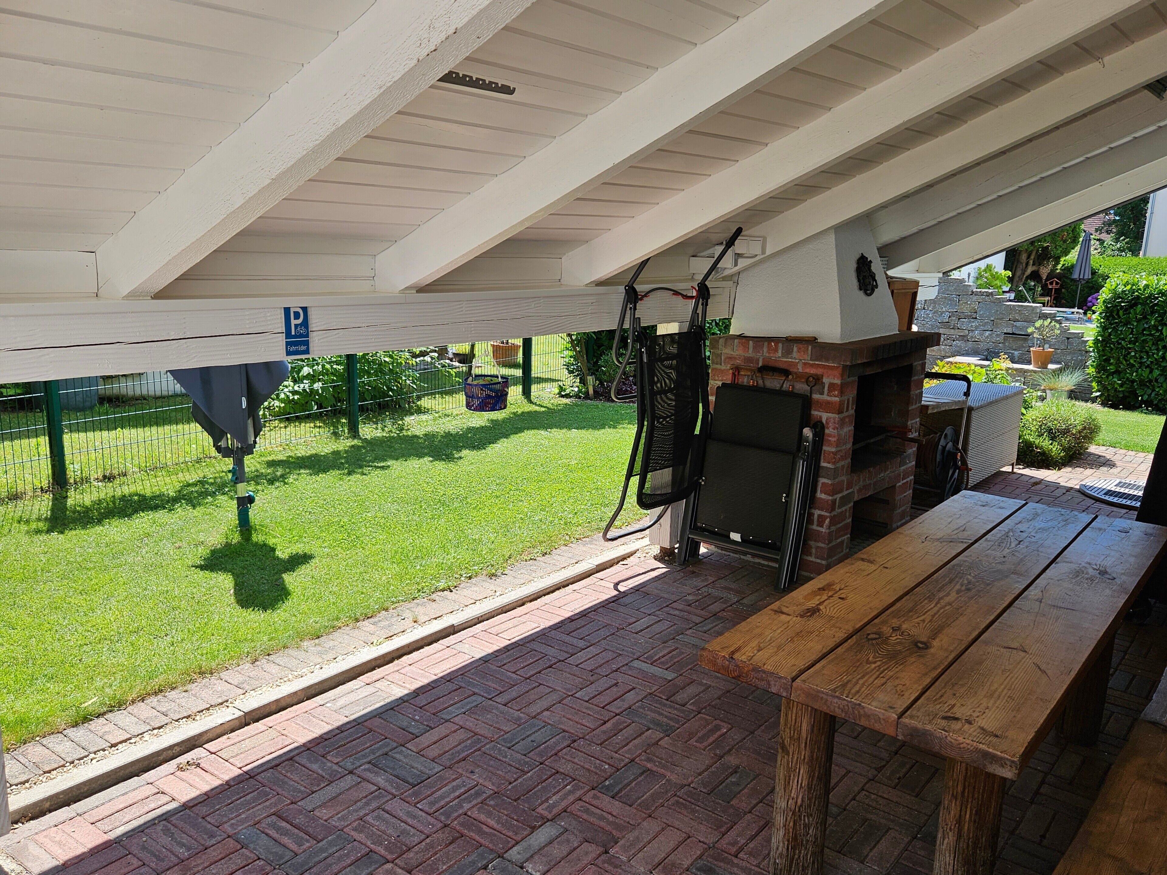 Un patio exterior con chimenea de ladrillo, banca de madera y un área cubierta con techo.