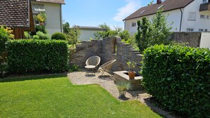 Een verzorgde tuin met een stenen muur, twee rieten stoelen en een kleine plant in een pot.