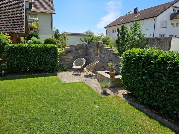 A well-maintained garden with a stone wall, two wicker chairs, and a small potted plant.