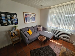 A living room with a grey sectional sofa, a small wooden side table, a black rug, and a radiator.