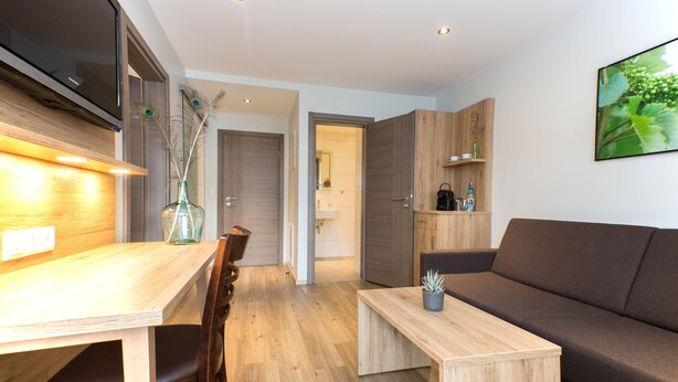 A modern living space with a wooden dining table, a sofa, and a TV mounted on the wall. - Apartment 1 with Balcony and Wi-Fi (Haslach im Kinzigtal)