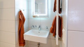 Een badkamer met een witte wastafel, een spiegel met verlichting en meerdere handdoeken.