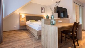 Een moderne slaapkamer met een bed, nachtlampjes, een televisie, een bureau en een stoel.