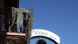 Een bord met de tekst 'Vino Veritas', een hangplant met beplanting en een decoratieve metalen sculptuur.