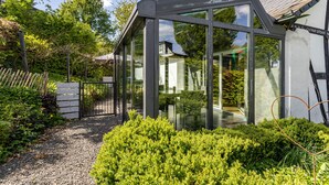 Une structure moderne en verre, dotée d’une ossature métallique, entourée de verdure et bordée d’un chemin de gravier.