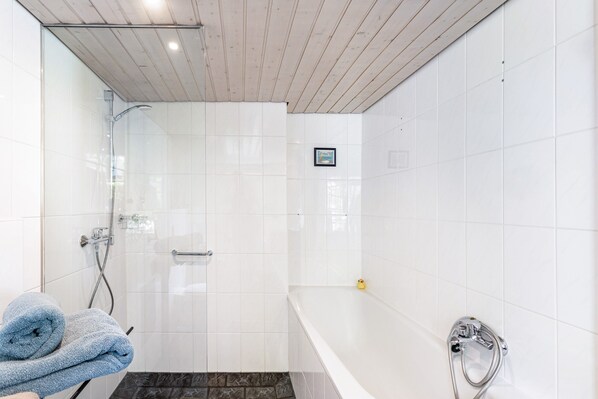 Een badkamer met een douche met glazen wand, een bad en een handdoekrek met handdoeken.