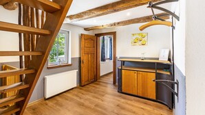 Un escalier en bois, une porte en bois, une fenêtre, un radiateur, un meuble et un luminaire suspendu.