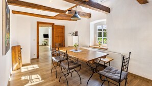 Un vaste espace dédié à la salle à manger, avec une table et des chaises en bois, des poutres apparentes, un luminaire suspendu et une vue par la fenêtre.