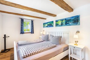 A bedroom with a bed, checkered bedding, a nightstand, a lamp, and two abstract paintings on the wall.