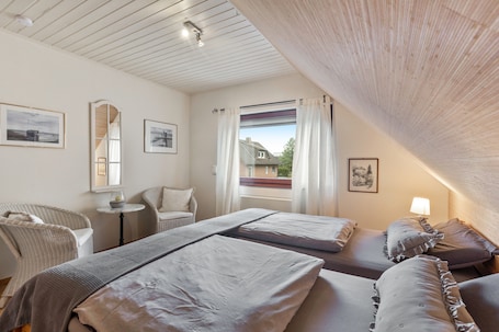 A bedroom with two beds, a chair, a small table, and a window with curtains.