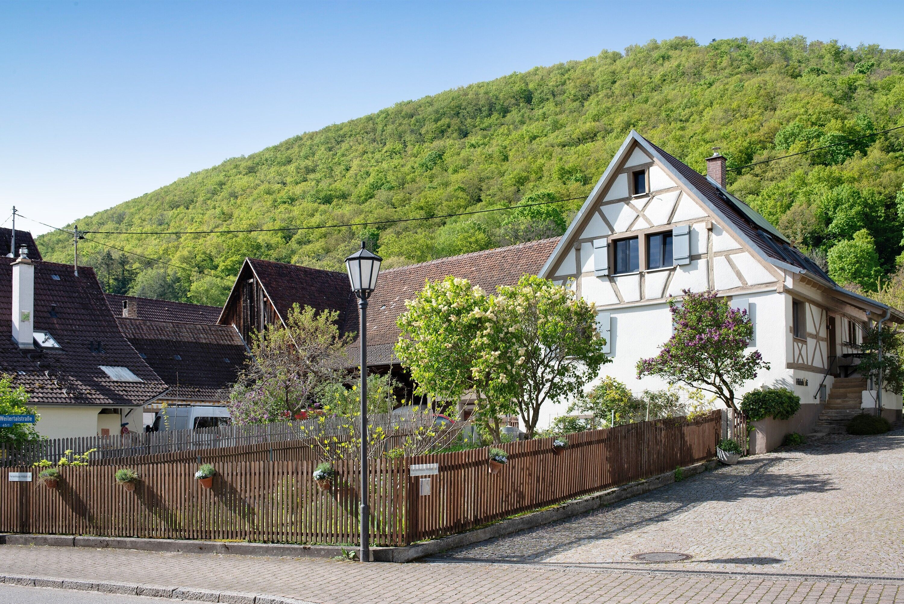 A traditional European house with a sloped roof, a wooden fence, and a paved street.