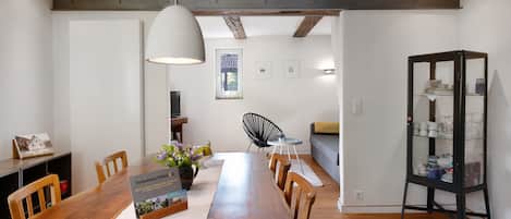 A dining area with a wooden table, chairs, a pendant light, a bookshelf, and a window with a view.