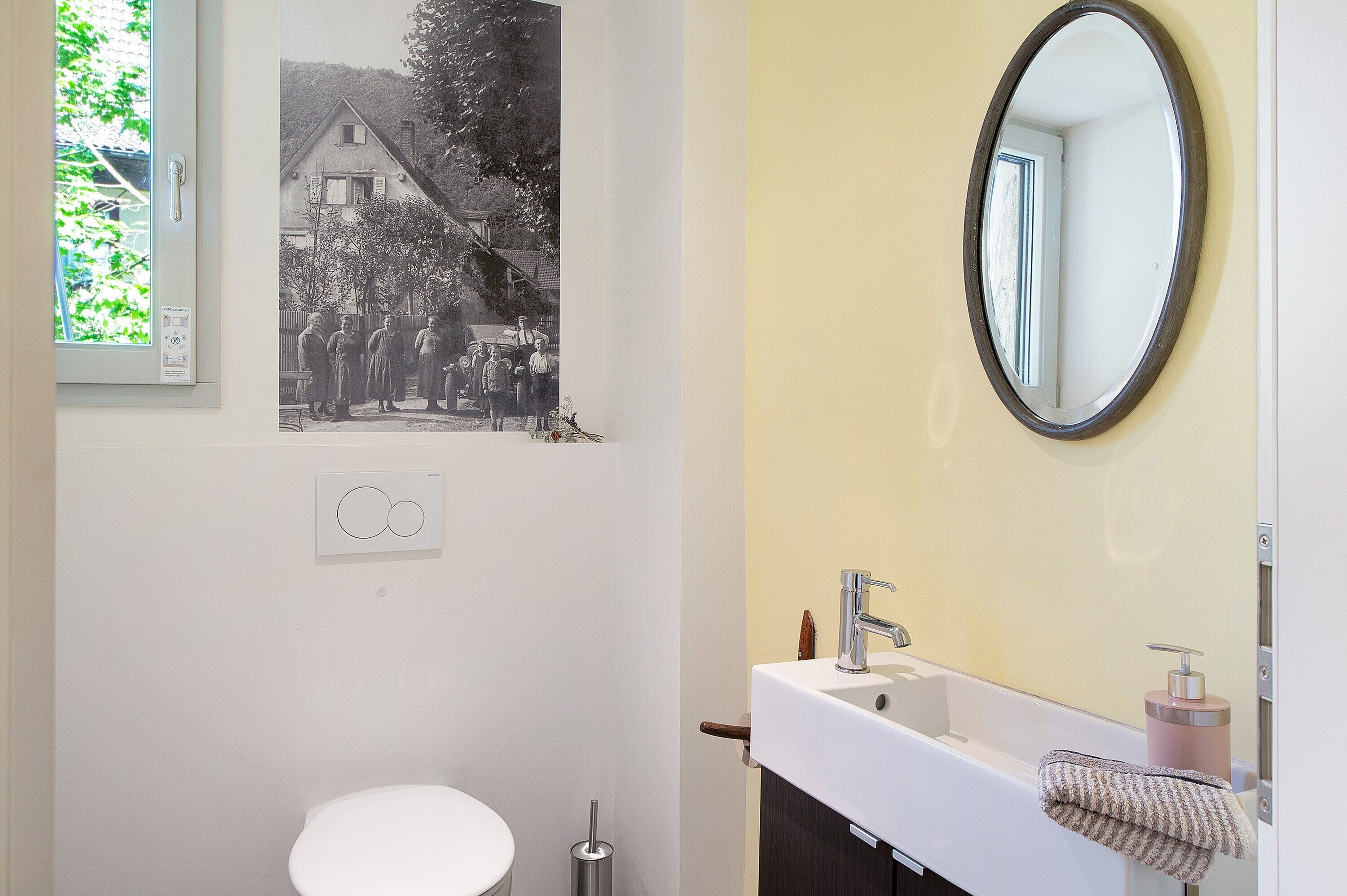 A bathroom with a toilet, sink, mirror, and a wall-mounted light switch.