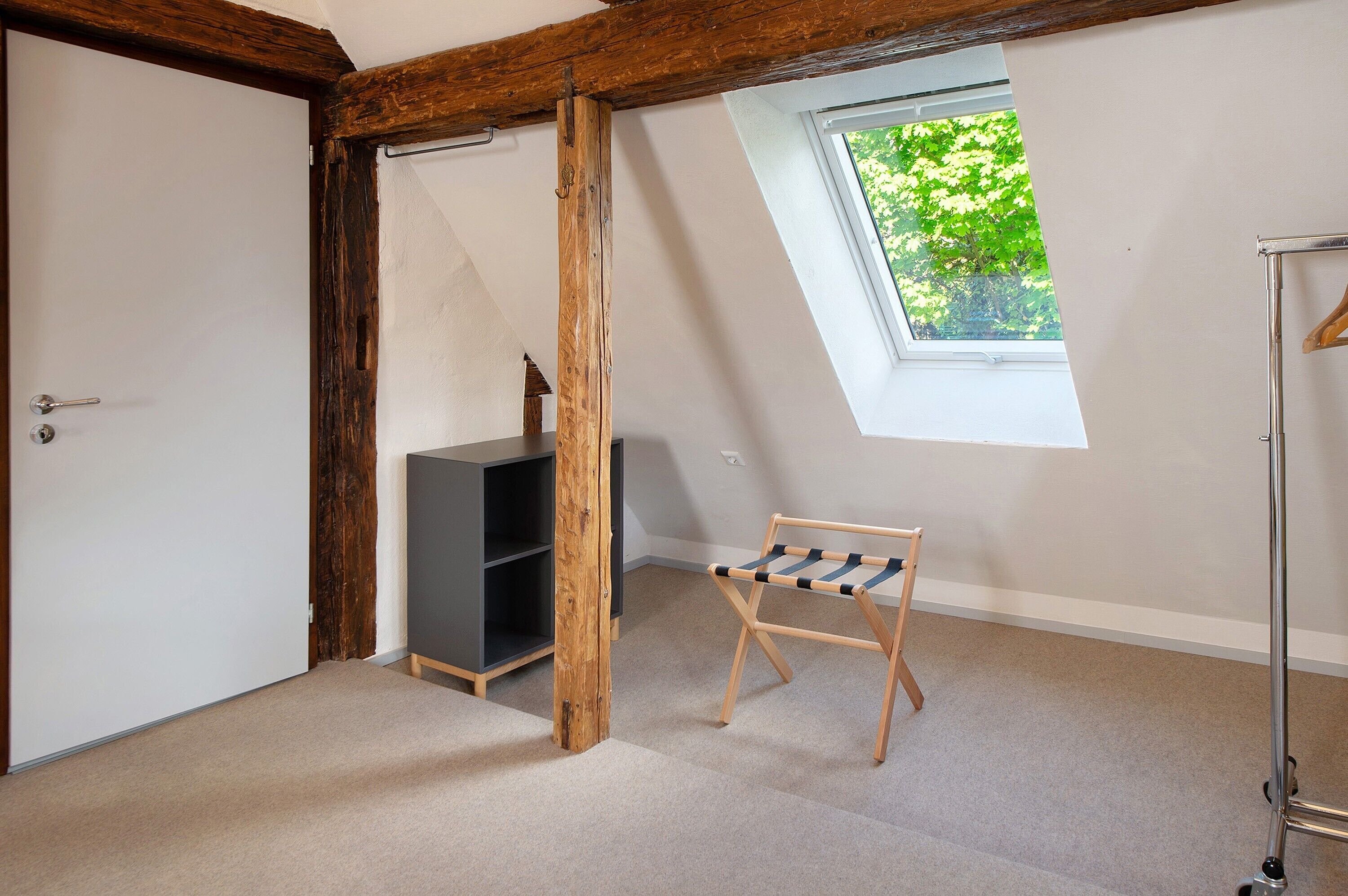 Une pièce dotée d’une lucarne, d’un plafond avec poutres apparentes, d’un meuble de rangement gris et d’un banc en bois.