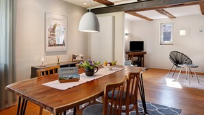 Un comedor con mesa de madera, sillas, lámpara colgante, televisor y ventana.