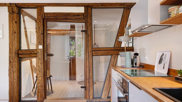 Una cocina con vigas de madera, un ventanal de vidrio hacia un patio y electrodomésticos modernos.