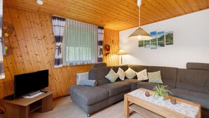 Habitación con paneles de madera, un sofá, un televisor sobre un mueble bajo, una mesa con una planta y una lámpara fijada a la pared.