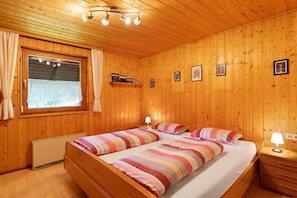 Ein Schlafzimmer mit Holzwandverkleidung, einem Bett, Nachttischlampen, einem Fenster mit Vorhängen und gerahmten Bildern an der Wand.