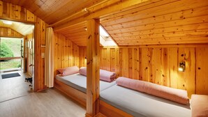 Interior de una cabaña de madera con dos camas, un tragaluz y vistas al exterior.