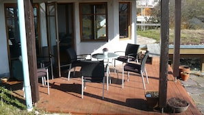 Un patio cubierto con una mesa, sillas y una ventana, y vistas del entorno.