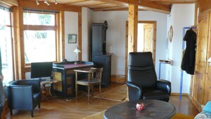 Una sala de estar acogedora con techo de madera, un escritorio con computadora, un sillón de cuero negro, una mesa de centro redonda y un sofá.