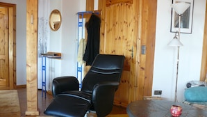 Una habitación con un sillón de cuero negro, una mesa redonda con un objeto rojo y paredes de madera.