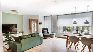 A modern living room with a green sofa, a dining table with chairs, a TV, and a large window with curtains. - Holiday Apartment 'Waldfeeling' with Private Terrace and Wi-Fi (Brilon)