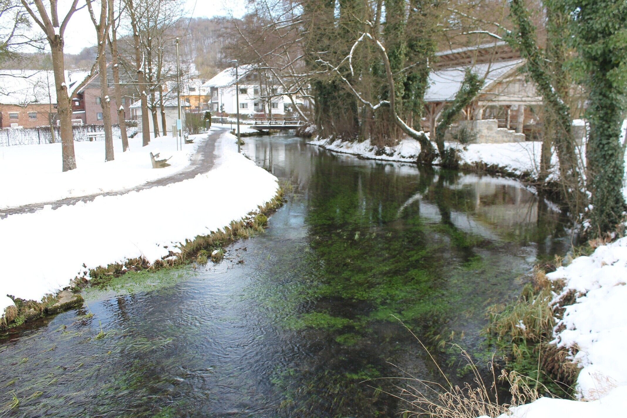 A snow-covered river with trees and buildings in the background.