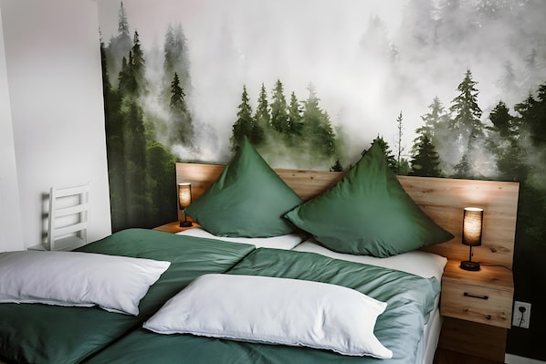 A bed with green and white bedding, a nightstand with a lamp, and a wall mural of a forest.