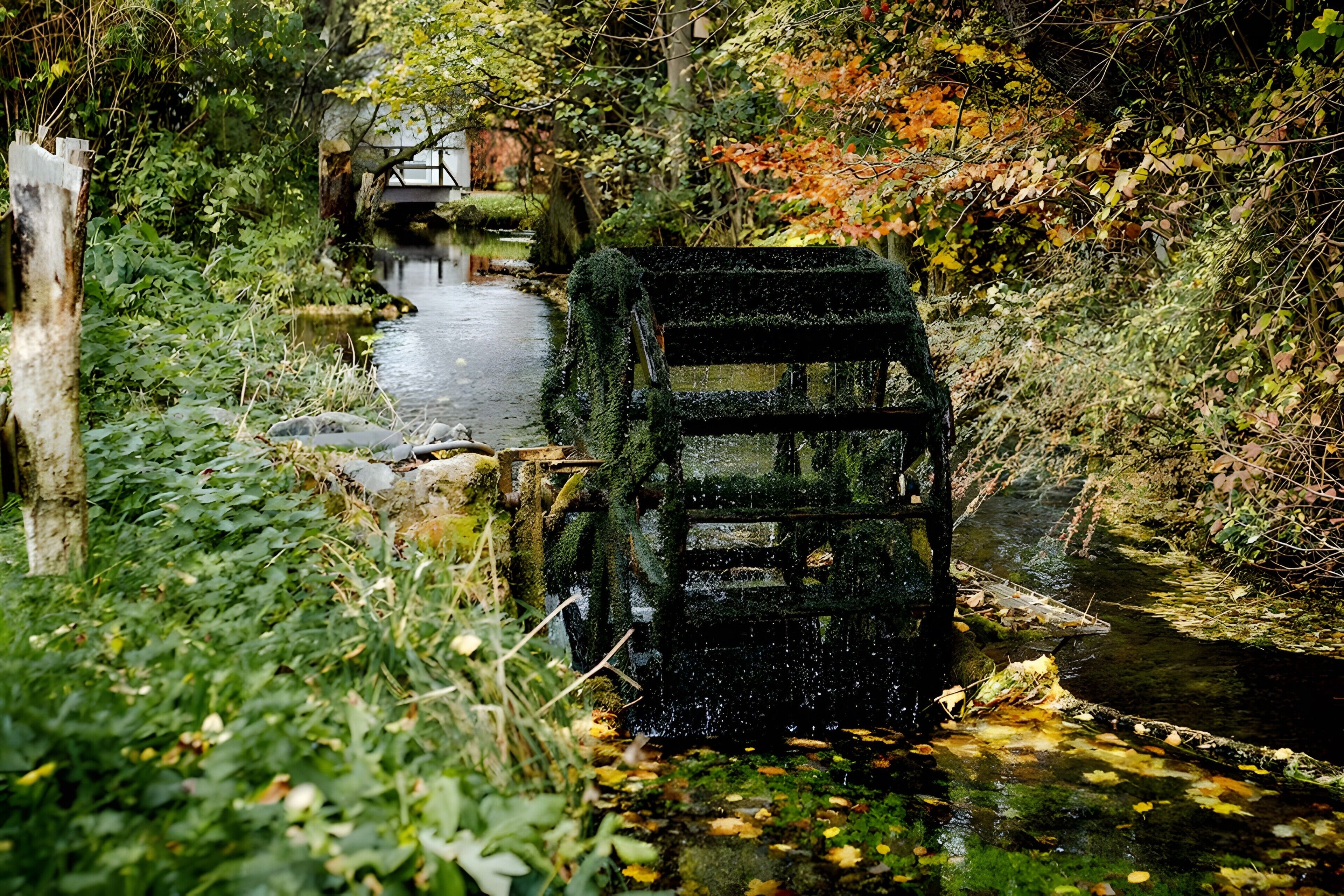 A rustic water wheel in a lush, green environment with a bridge in the background.