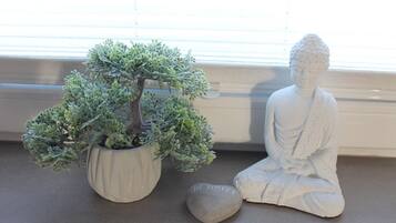A bonsai tree in a pot, a seated Buddha statue, and a smooth stone with 'BE HAPPY' inscribed on it.