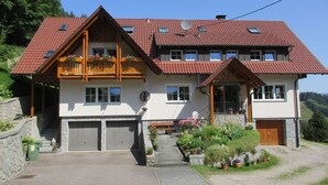Une maison à deux étages, avec un toit recouvert de tuiles rouges, des balcons en bois et un mur en pierre.