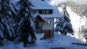 Une maison recouverte de neige, avec des fondations en pierre, un revêtement extérieur en bois et une porte d’entrée bien visible.
