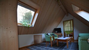 Une pièce avec un plafond en pente, une télévision, une table avec des chaises et un canapé.