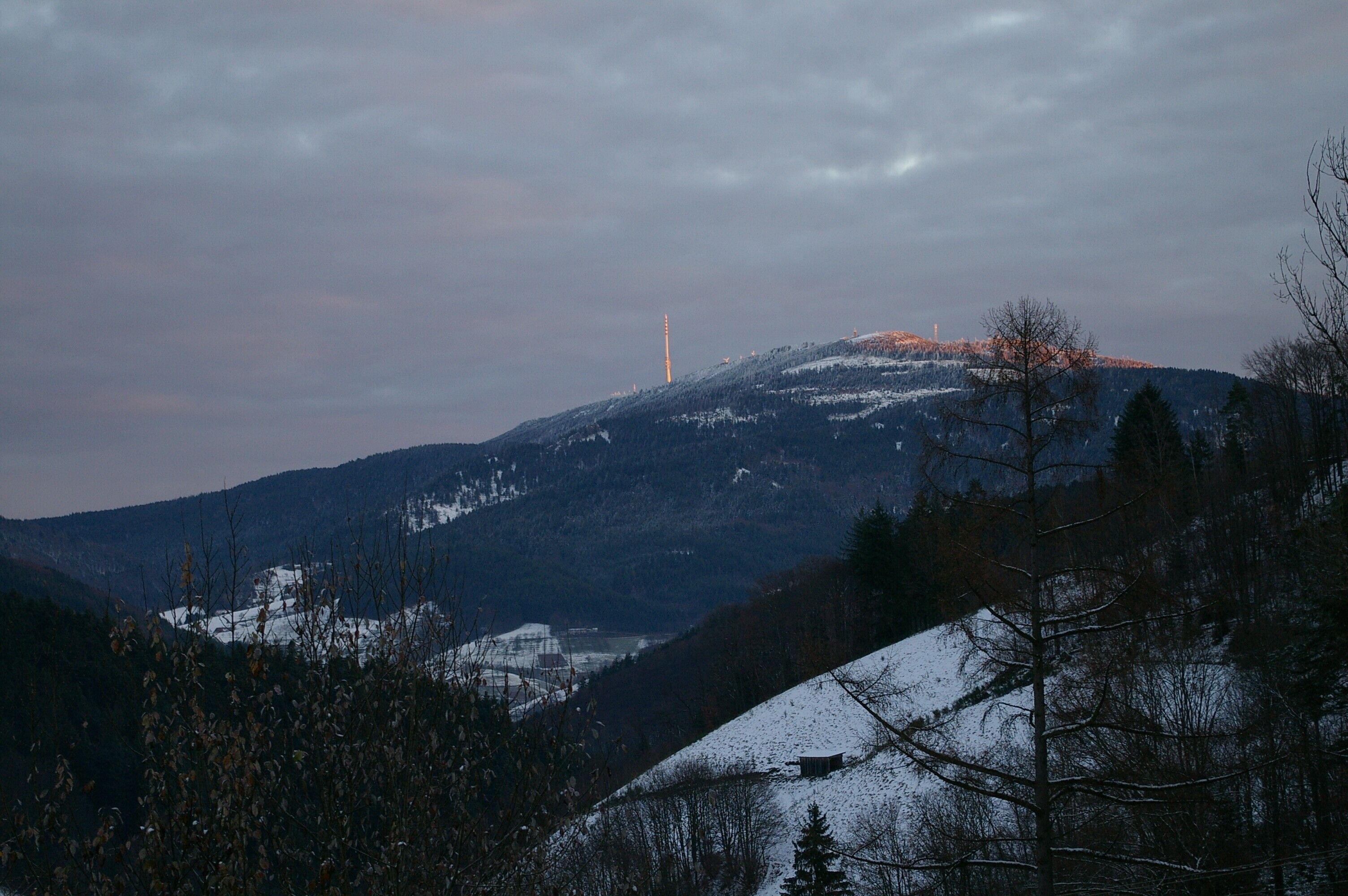 A mountainous landscape with a snow-covered peak, a distant tower, and sparse vegetation.