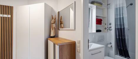 Un baño moderno con lavamanos, inodoro y zona de ducha blancos.