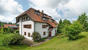 Ein zweistöckiges Haus mit geneigtem Dach, weißen Außenwänden und braunen Fensterläden.