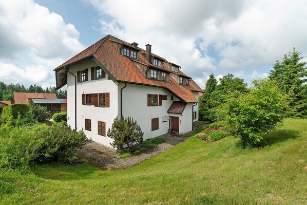 A two-story house with a sloped roof, white exterior walls, and brown shutters.