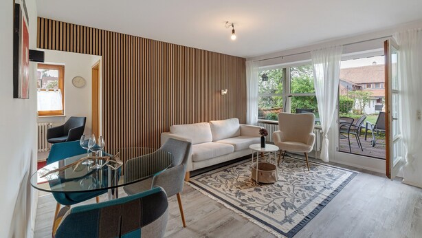 Ein modernes Wohnzimmer mit einer Couch, Sesseln, einem Glastisch und einem gemusterten Teppich.